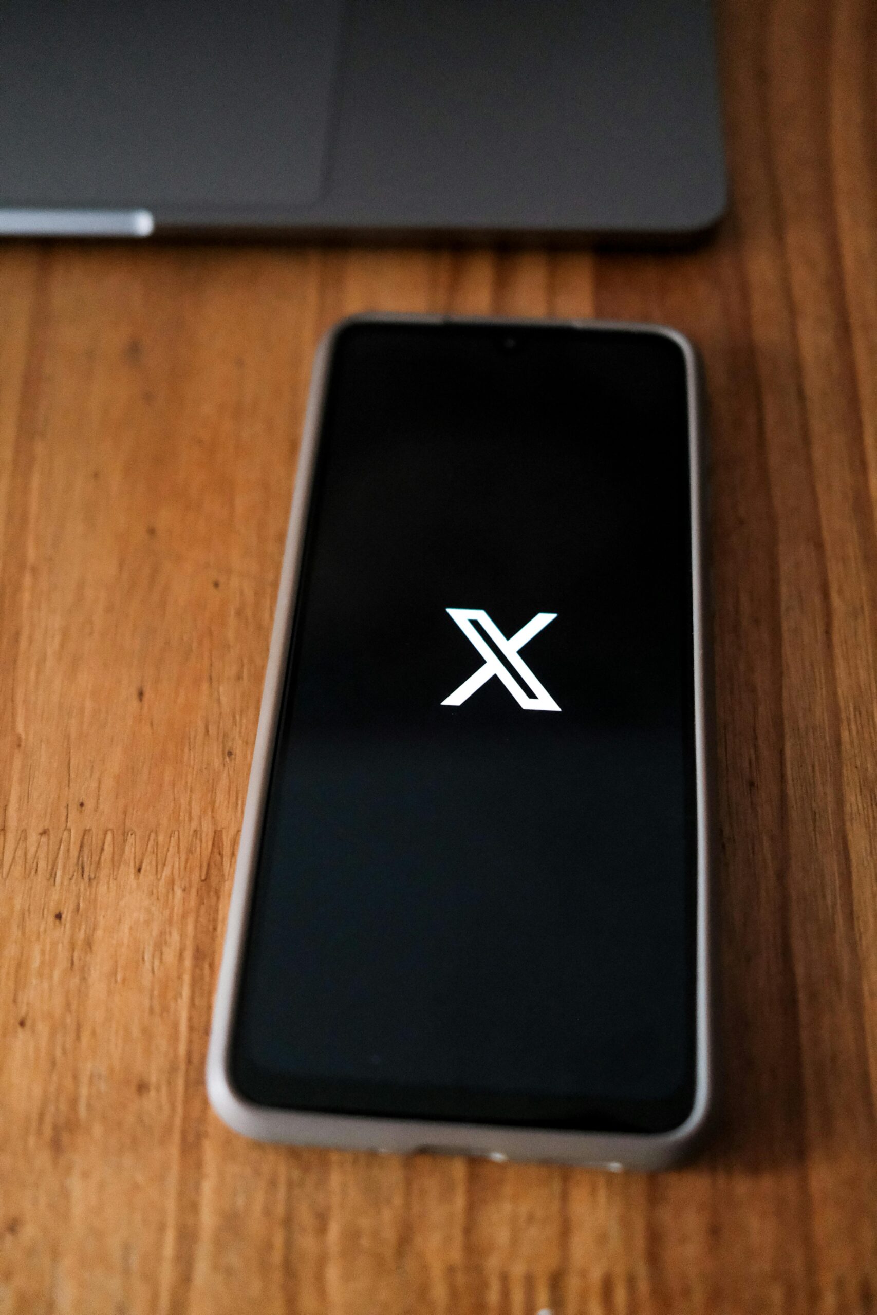 A smartphone showing a prominent social media icon, placed on a wooden desk.