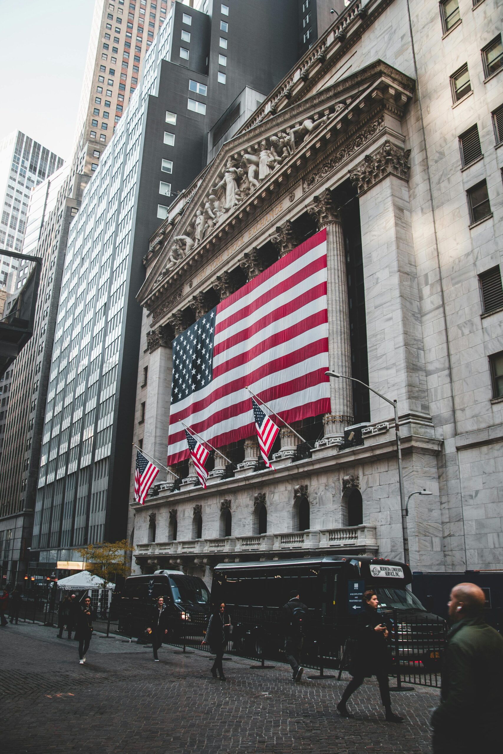 The New York Stock Exchange adorned with large American flags, bustling street life below.