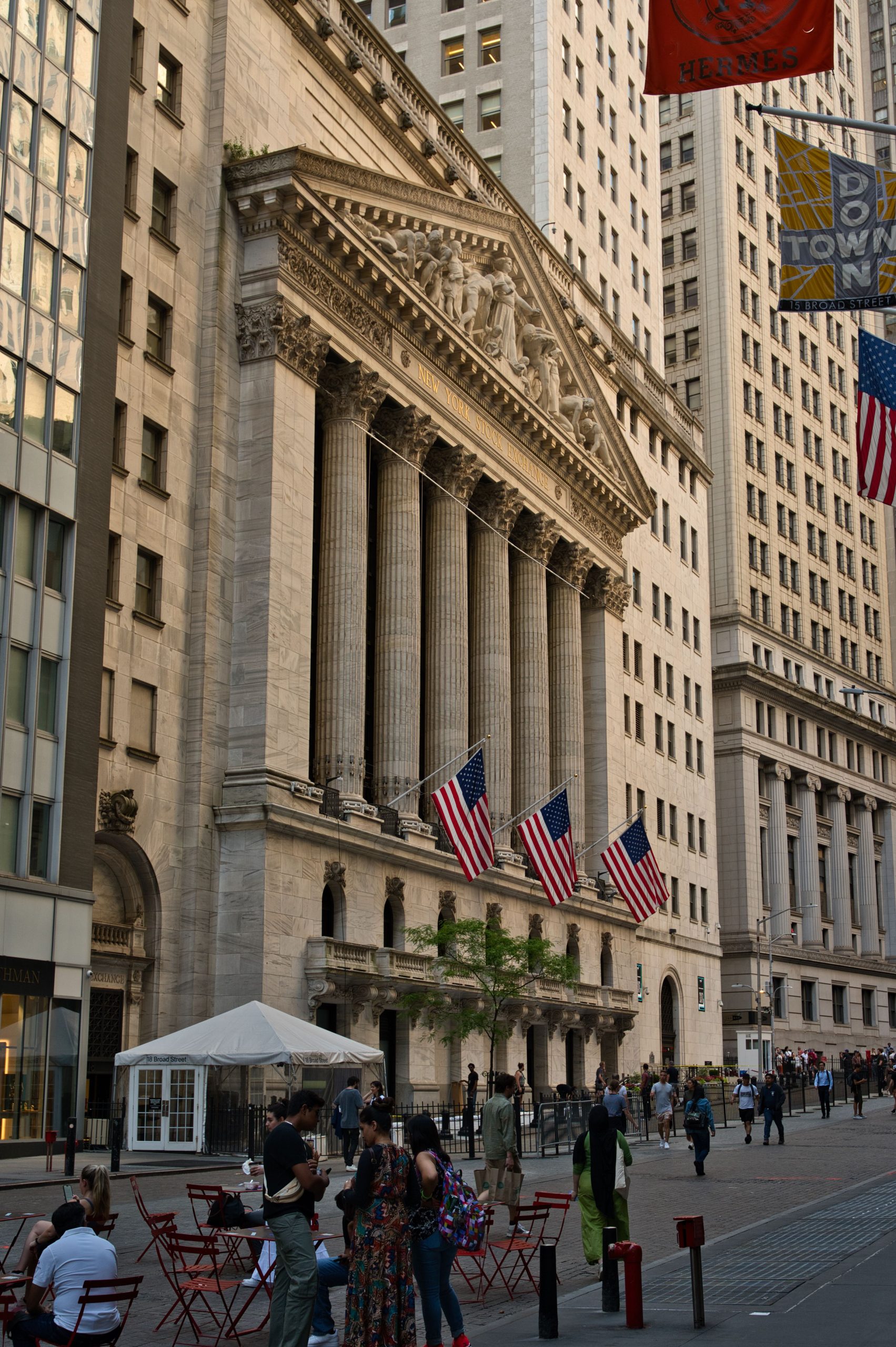 Iconic New York Stock Exchange on Wall Street with pedestrians and flags.